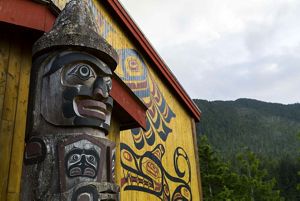 A wooden carved piece of artwork sits in front of a brightly painted building next to a mountain.