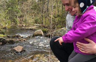 Eileen Bader Hall holds her daughter while they look into a flowing stream.
