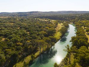 A turquoise river cuts between an expanse of hilly land dotted with green trees.