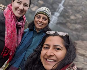 Three women standing in front of a waterfall.