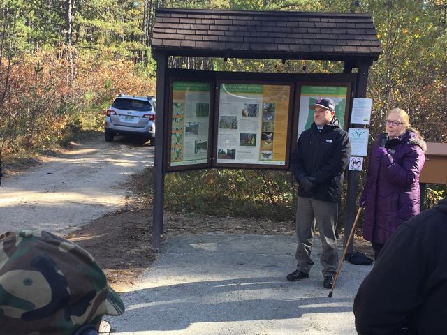 Two people stand outside at a trailhead and talk to a group of people.