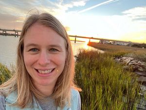 The sun sets behind a woman smiling at the camera.