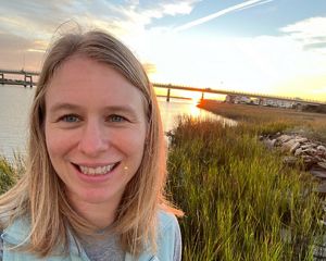 The sun sets behind a woman smiling at the camera.