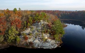 A high granite outcrop juts out into a pond surrounded by oak forest in the fall. 