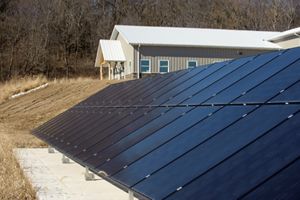 A bank of solar panels in front of a tan metal building with a white metal roof.
