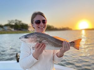The sun sets behind a woman holding a fish.
