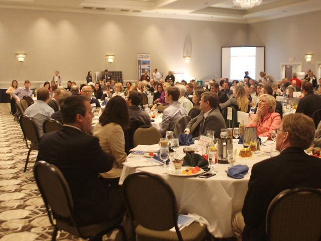 A large group of people are seated around round banquet tables in a hotel ballroom.