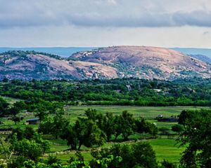 A dome of pink rock towers over green fields with trees.