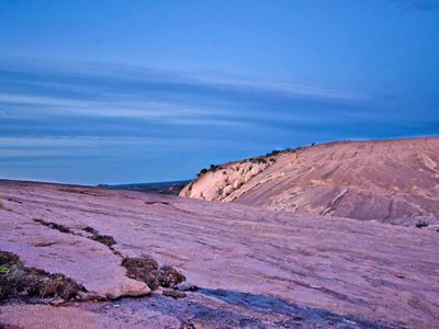 Un punto alto en que se ve un monte de granito rosa en primer plano al atardecer.