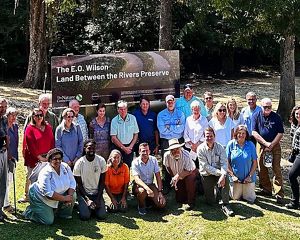 A group of people gather around a nature preserve sign.