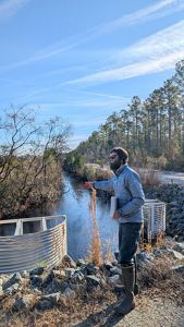 Eric Soderholm, a peatland restoration expert, gestures in front of a stream, where water is being held in a culvert to help rewet a nearby peatland in North Carolina.