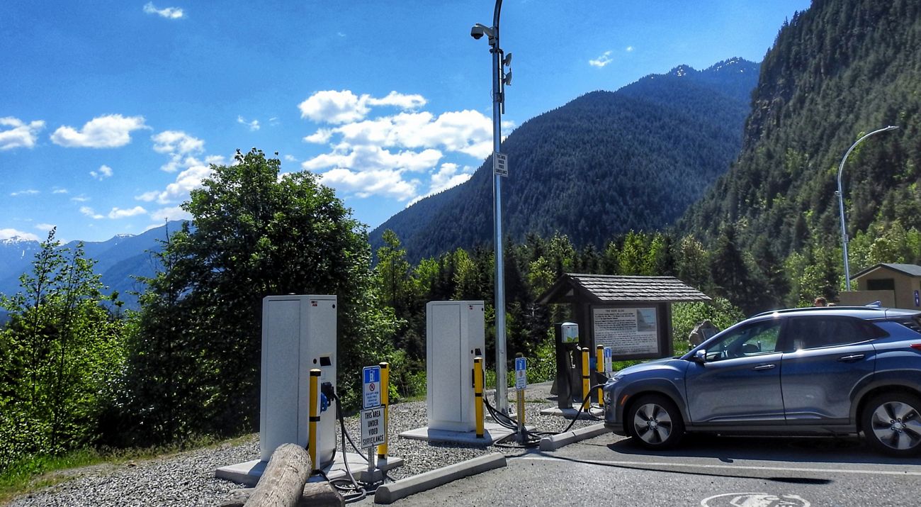 Un vehículo eléctrico está en una estación de carga en un paisaje montañoso de Columbia Británica.