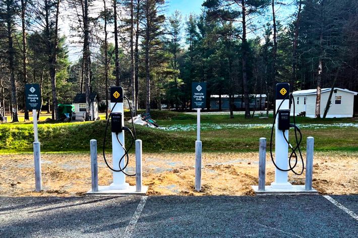 A white car sits in a lot plugged into an electric charging station.