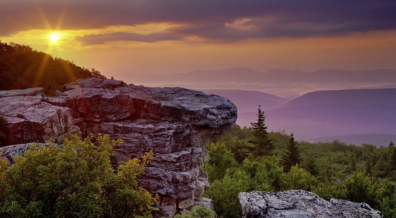 A rocky outcropping in the foreground and a mountain range with trees in the distance.