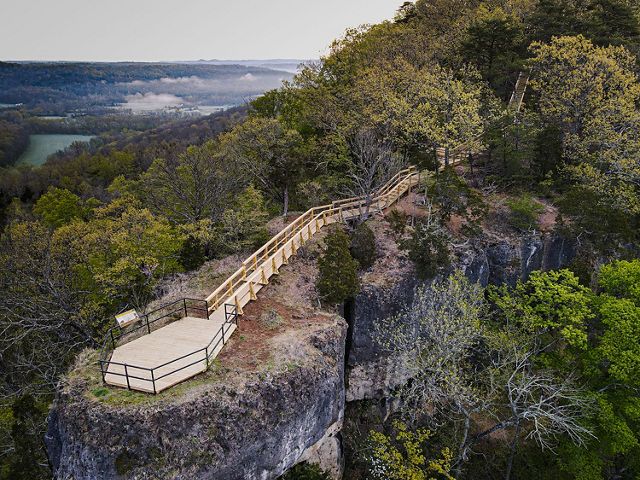A bird's eye view looking down on a wooden platform and trail that overlooks a breathtaking forest.