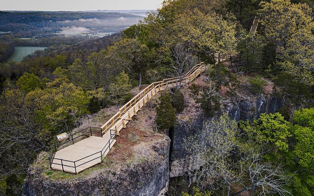 A bird's eye view looking down on a wooden platform and trail that overlooks a breathtaking forest.