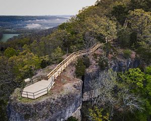 A bird's eye view of a wooden platform and trail that overlooks a breathtaking view of forest covered hills.