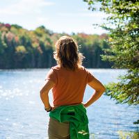 Woman looking into a lake with foliage in the background.