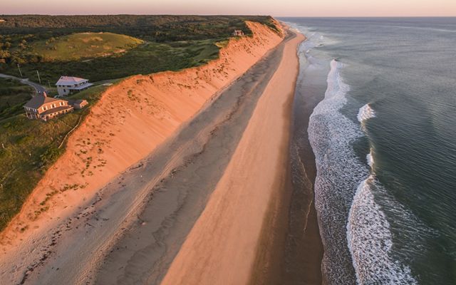 A high sand bluff is seen from above. Two houses sit within a few hundred feet from the edge of the bluff
