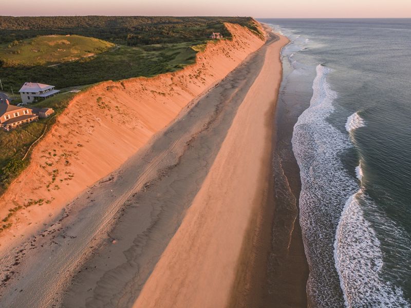 A high sand bluff is seen from above. Two houses sit within a few hundred feet from the edge of the bluff