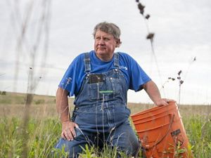 portrait of man in overalls sitting in a field with an orange utility bucket