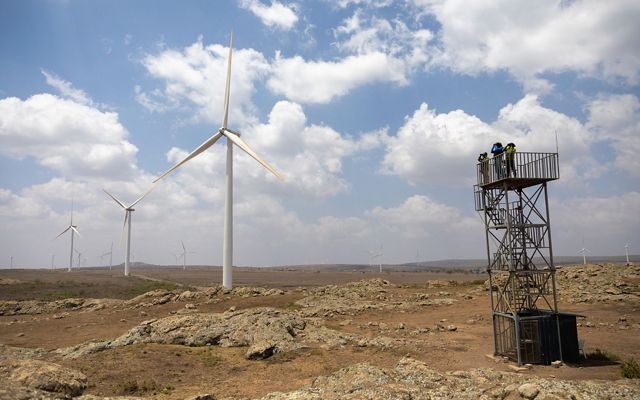 Bird observers surveying for birds from a tower; the tower stands in a vast landscape with several wind turbines standing nearby and in the distance.