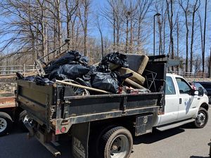 A large municipal truck parked in a parking lot is piled high with full black trash bags and large debris.