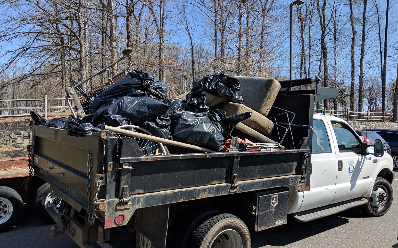 A large municipal truck parked in a parking lot is piled high with full black trash bags and large debris.