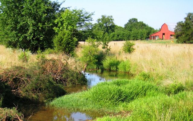 A small stream flows away from a red farmhouse.