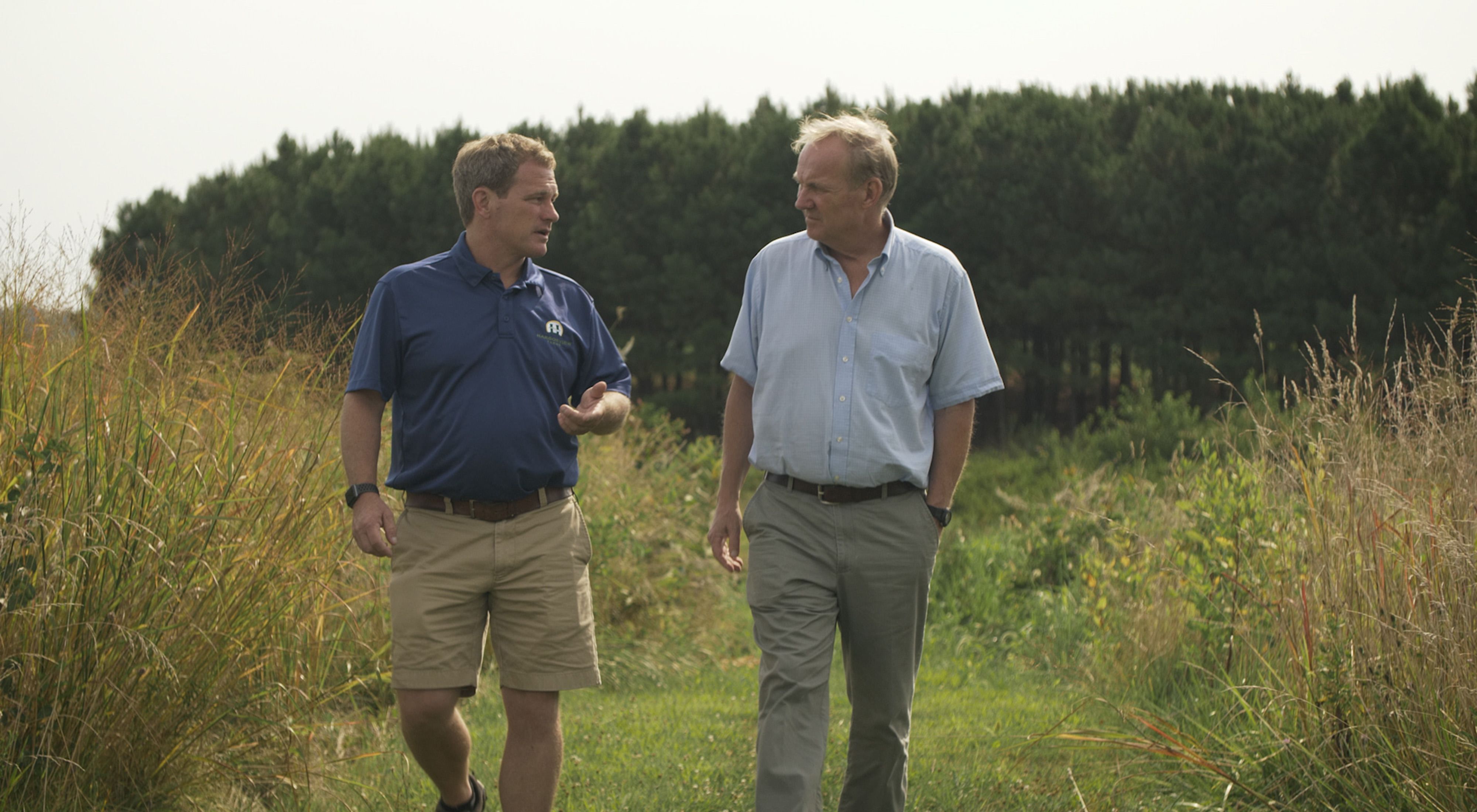 Farmer Trey Hill and landowner Joe Hickman walk through farm fields.