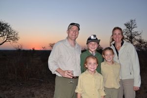A family smiles holding each other in from of a sunset in Africa. 
