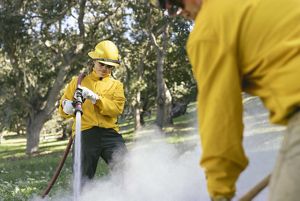 A woman in a yellow jacket holds a fire hose over her shoulder while she soaks ashes after a controlled burn.