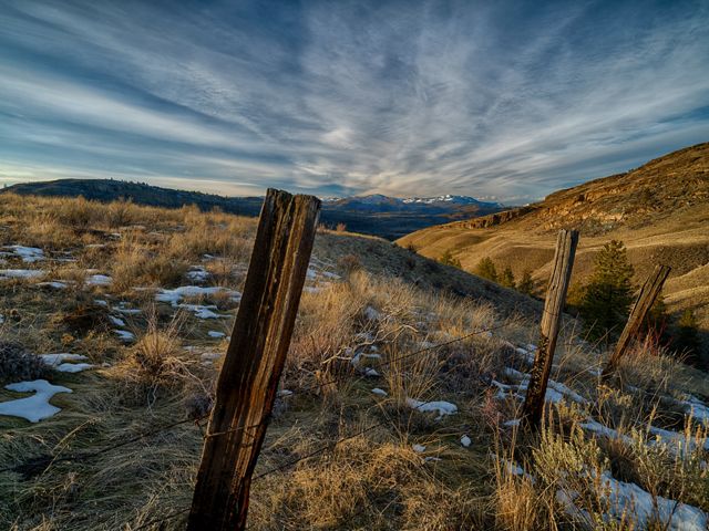 Photo showing an old fence in the foreground, with rolling grasslands behind it and the Tunk Creek Valley in the background.