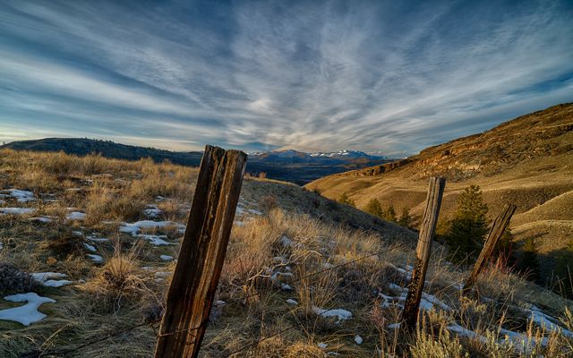 Photo showing an old fence in the foreground, with rolling grasslands behind it and the Tunk Creek Valley in the background.