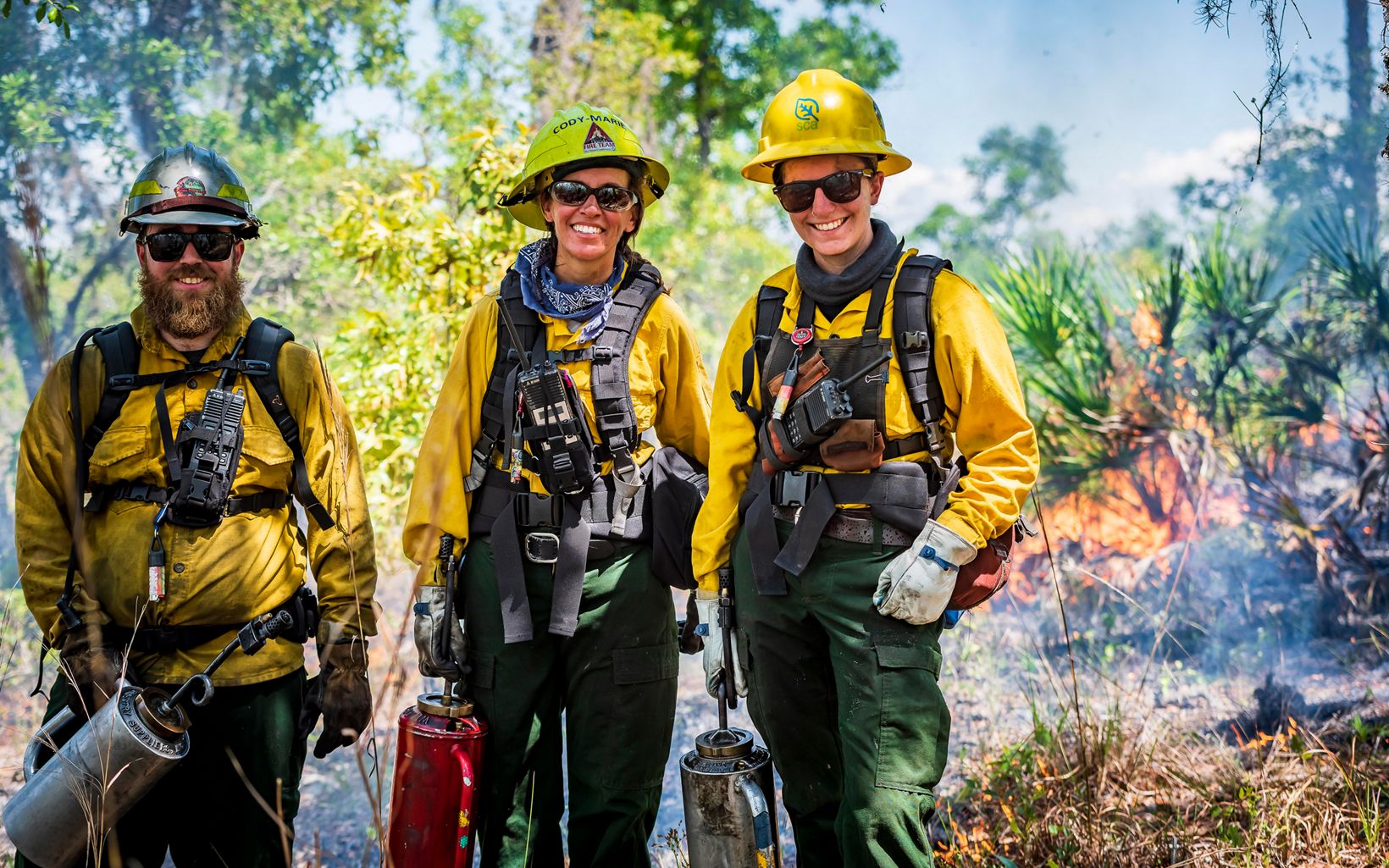 Three people in fire fighting outfits smile during a prescribed fire at Tiger Creek Preserve. 