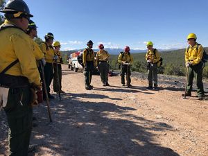 Several people in yellow prescribed fire gear and hardhats discuss plans.