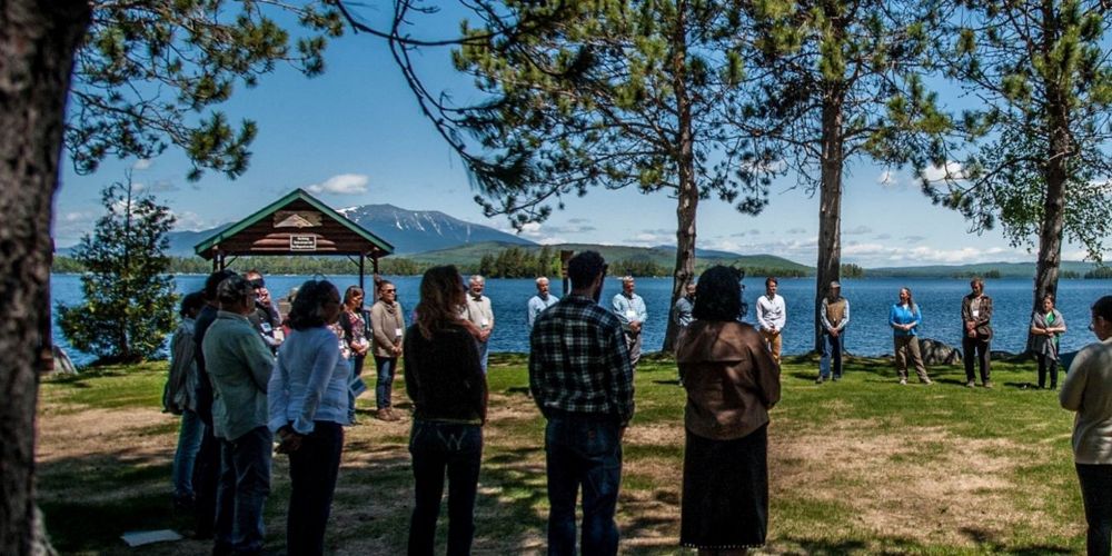 People stand in a circle with a lake behind them.