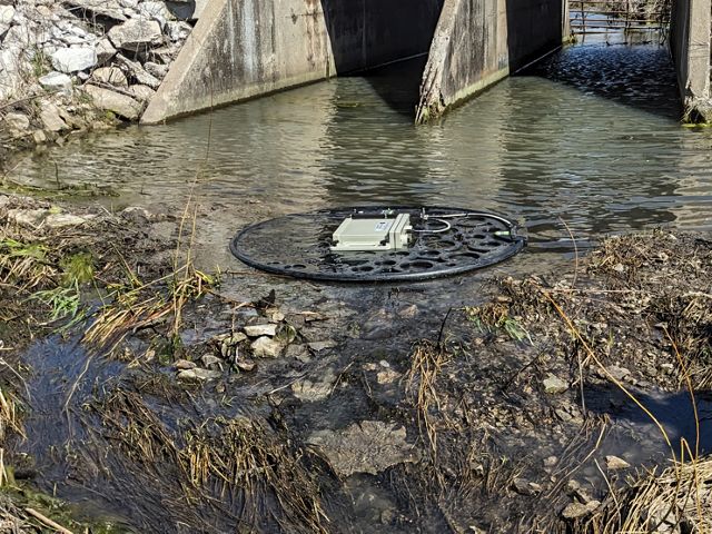 A round floating antenna placed just past a concrete culvert in a stream.