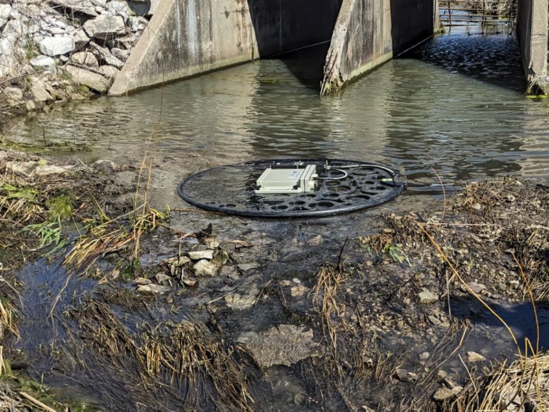 A round floating antenna placed just past a concrete culvert in a stream.