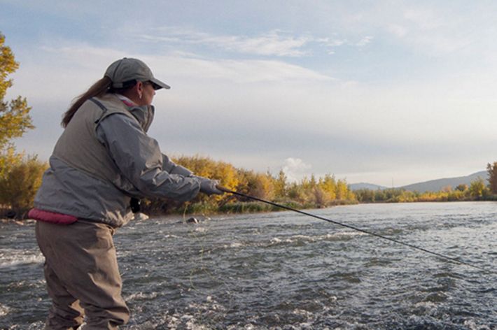 Photo of a woman fishing on an open stream.