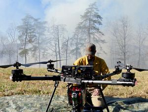 A large drone sits on the ground in front of a person kneeling to look at it.