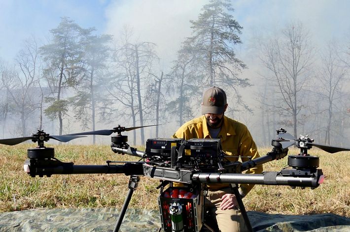 A large drone sits on the ground in front of a person kneeling to look at it.