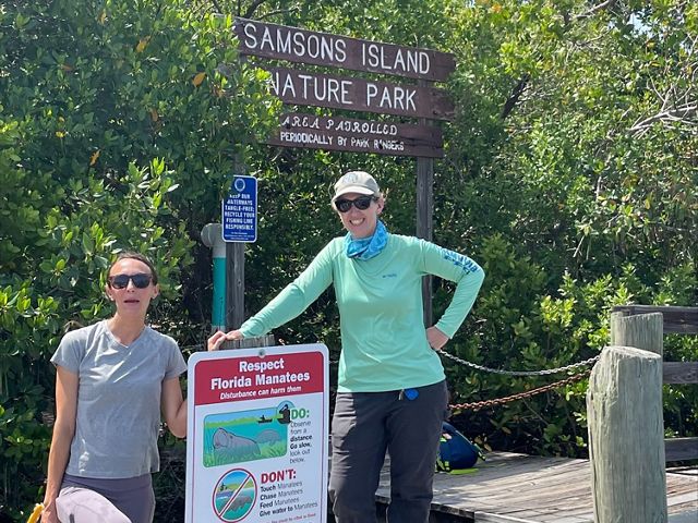 Two women stand on a board walk and next to a sign that brings attention to manatees in Florida waters.