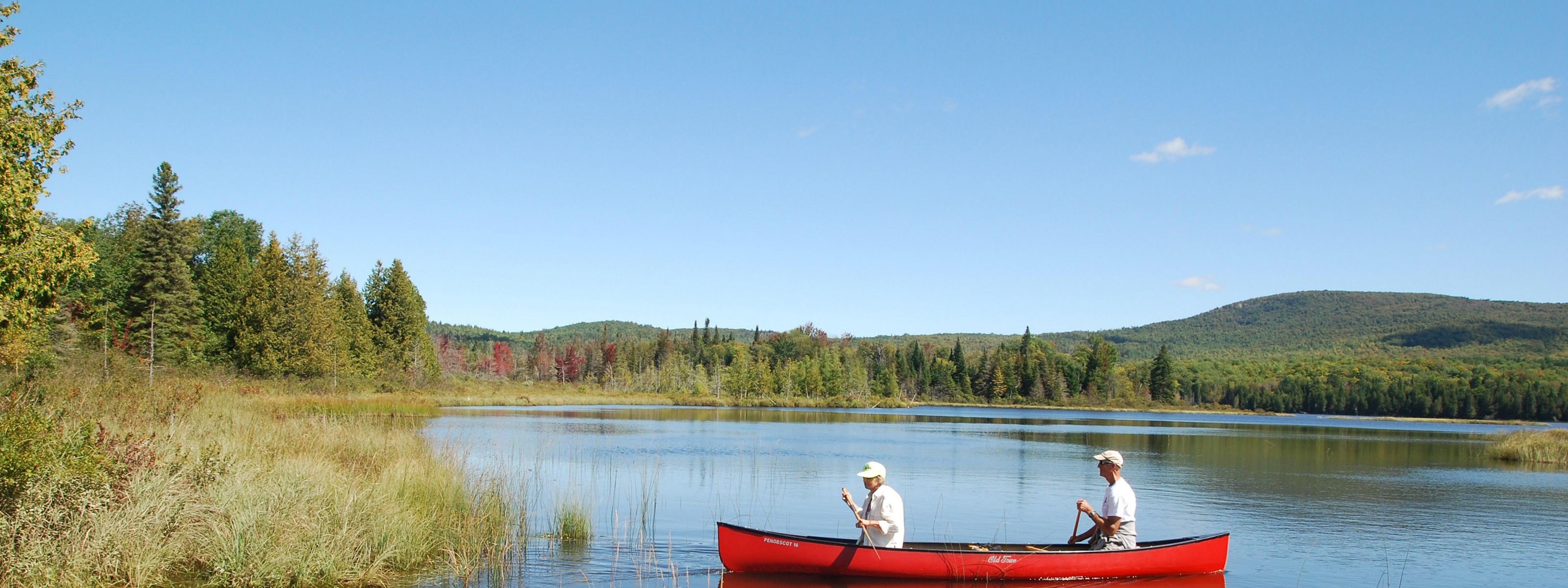 Two people paddle a red canoe on a pond with forested mountain slopes in the background.