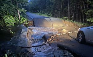 a car's headlights illuminates a partially washed-out road with a culvert underneath during a 2016 storm event.