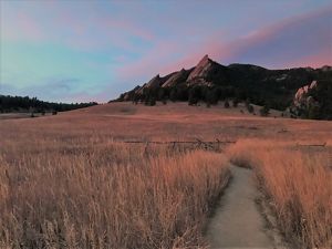 The sun sets over mountains and grasslands.