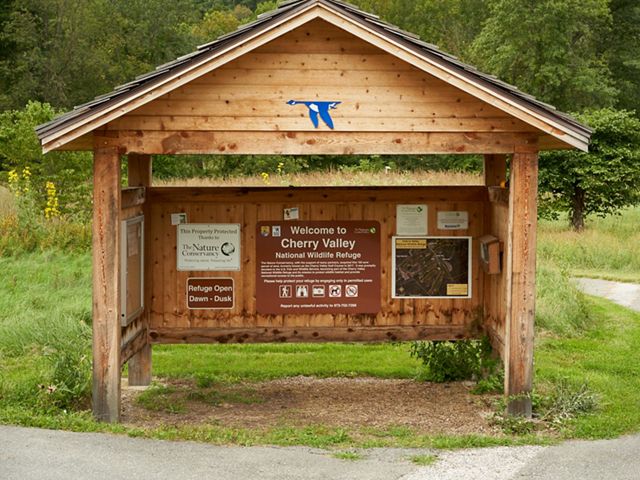 A wooden kiosk with several maps sits in front of a forest.