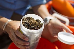 A person holds an open sample container filled with oyster shells, marine debris, and sediment collected during fieldwork on a boat.