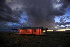 A cabin is lit up with red lights as evening turns to night in the desert.