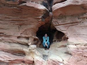 A woman kneels in the crevice of a canyon, smiling for the photo.